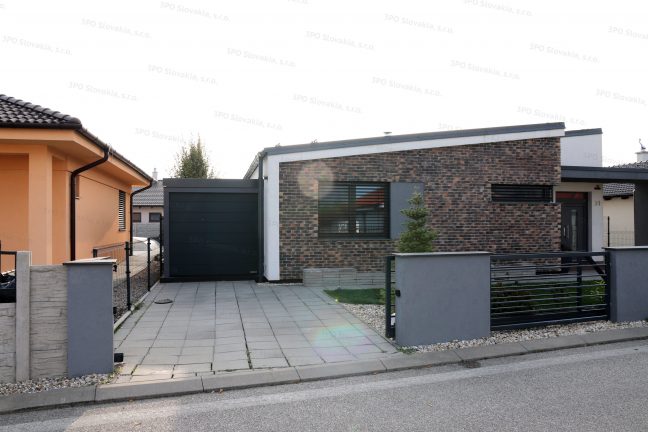 Montovaná garáž v tmavosivej omietke s antracitovou garážovou bránou pri rodinnom dome