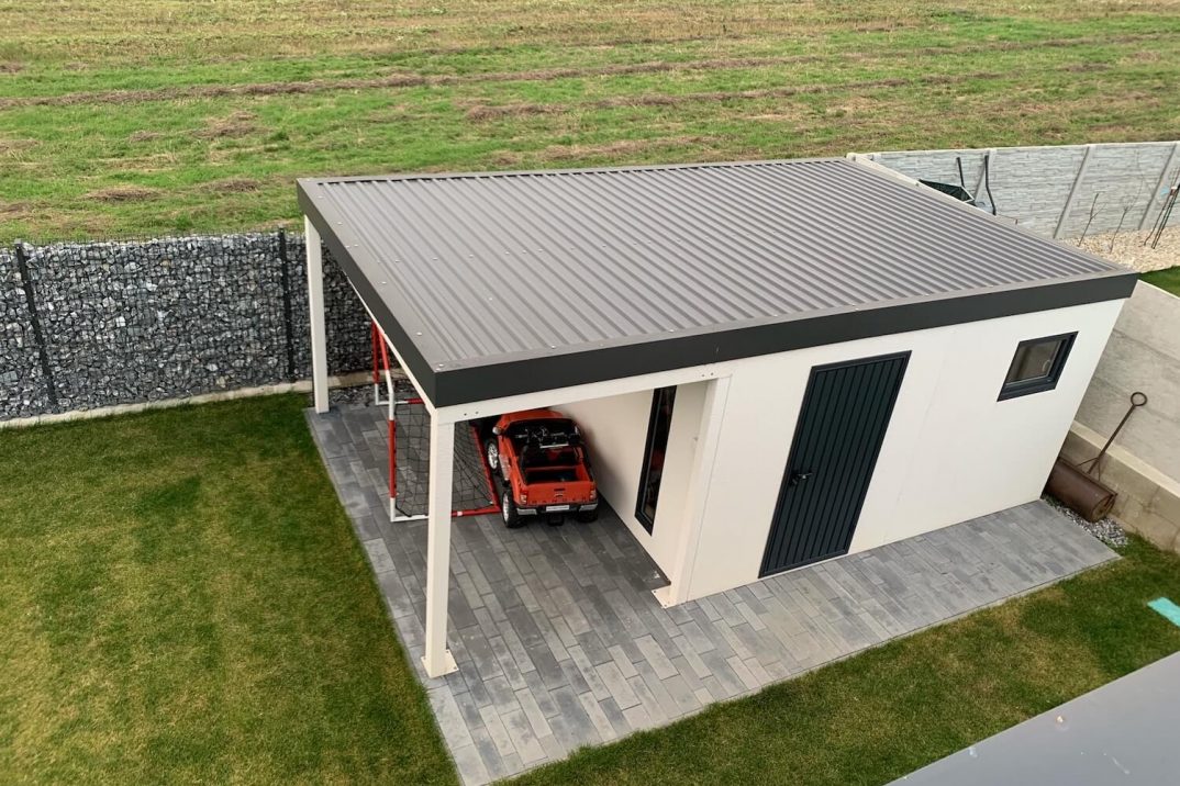 Pohľad zhora na záhradný domček s bráničkou a hracím autom pod prístreškom