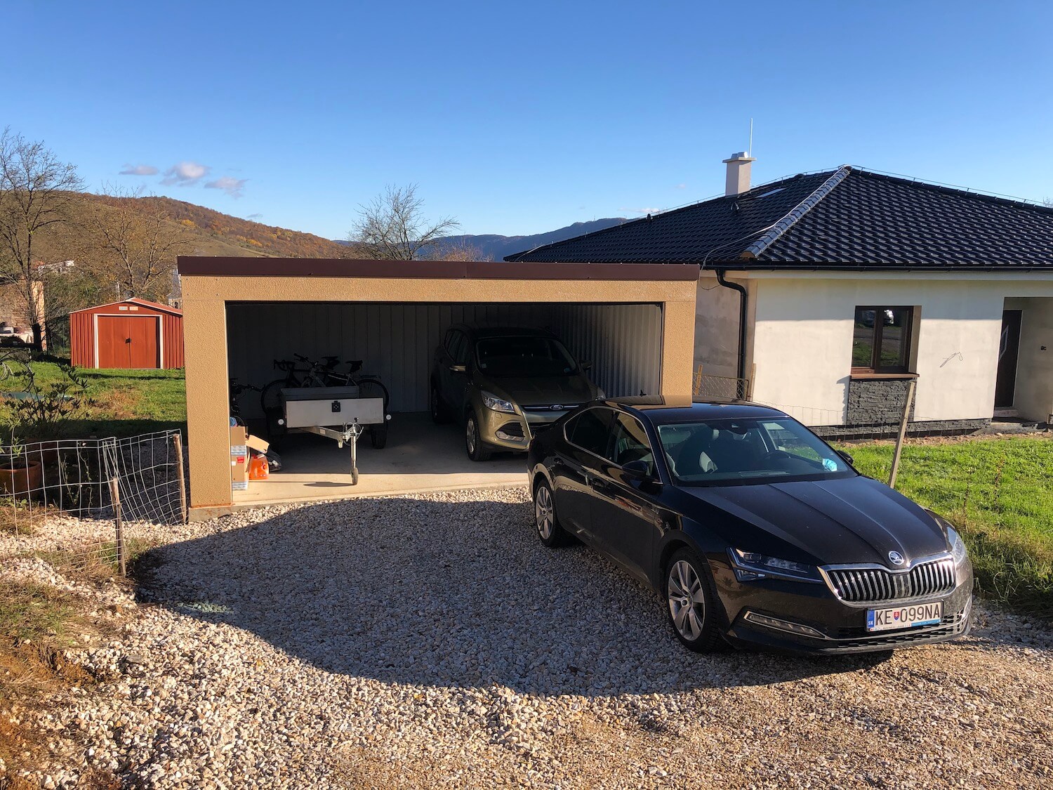 Auto pred otvorenou garážou s autom a bicyklami