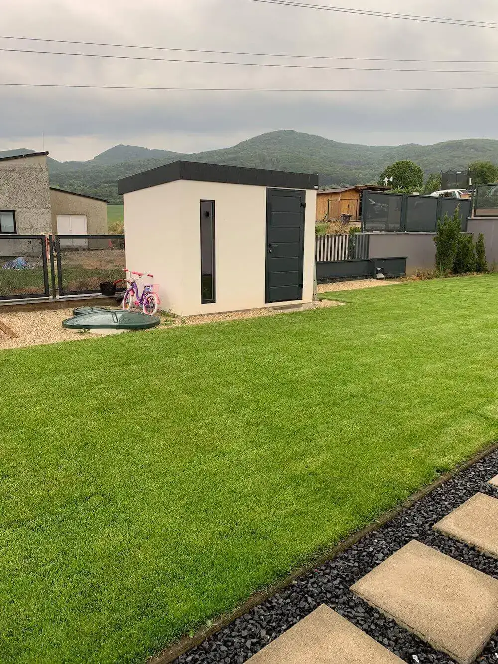 Ružový detský bicykel opretý o záhradný domček v bielej omietke