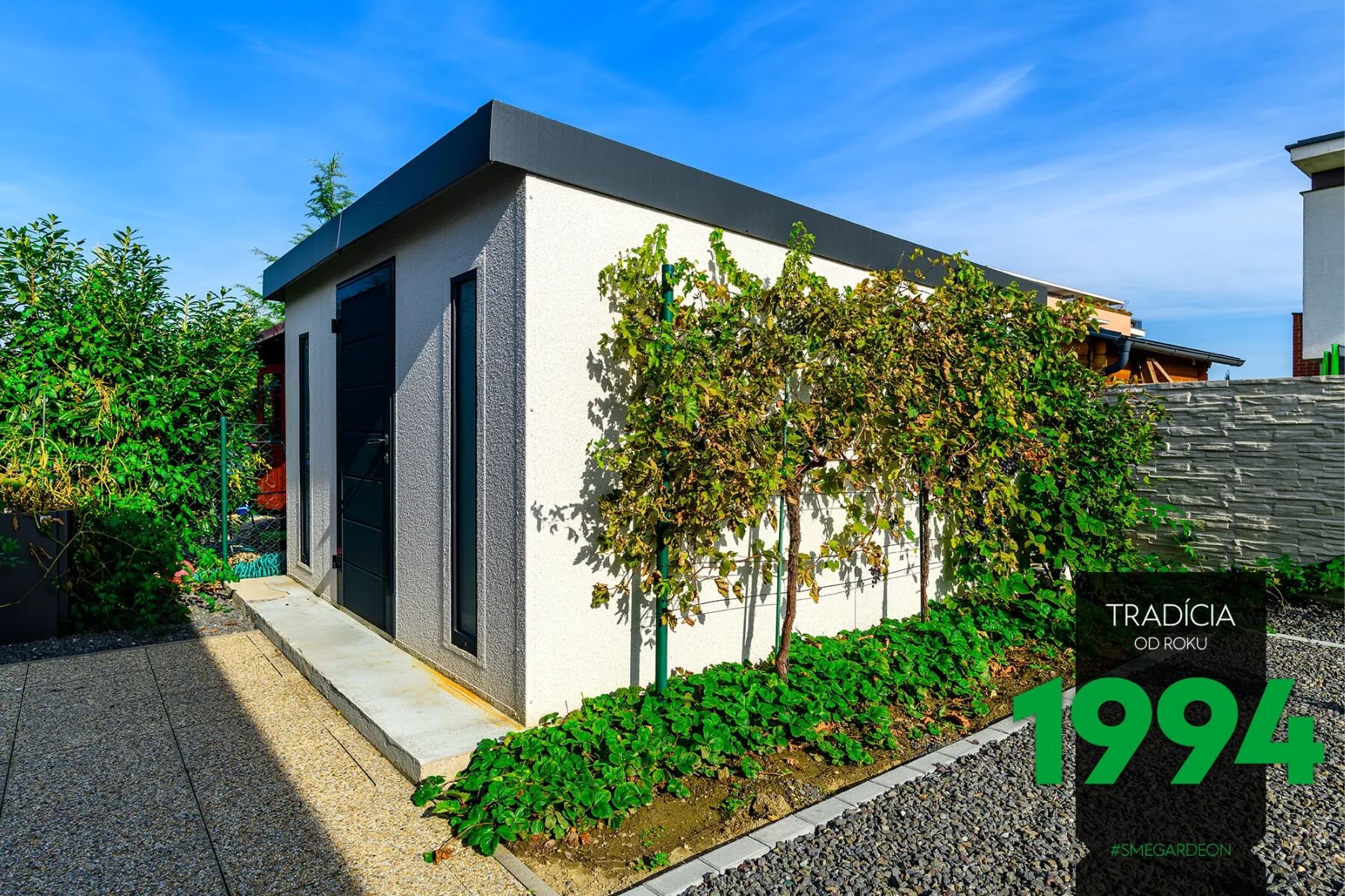 Záhradný domček v bielej omietke a stromčeky s oporou.