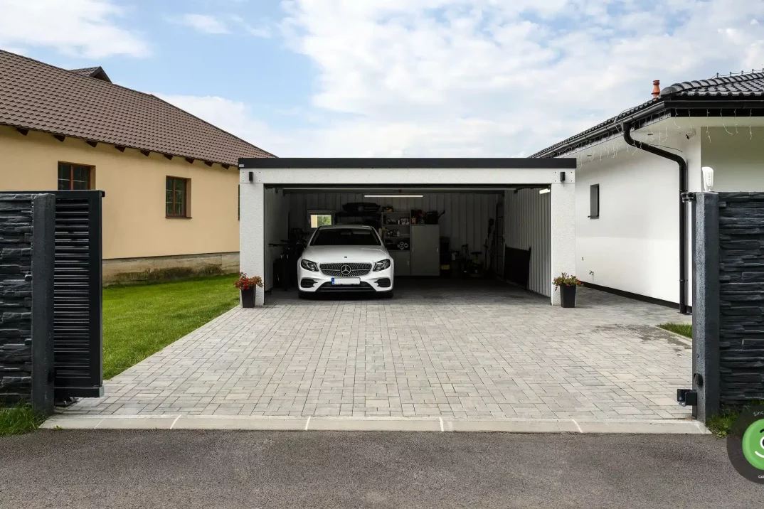 Garáž s pultovou strechou pri bielom rodinnom dome.