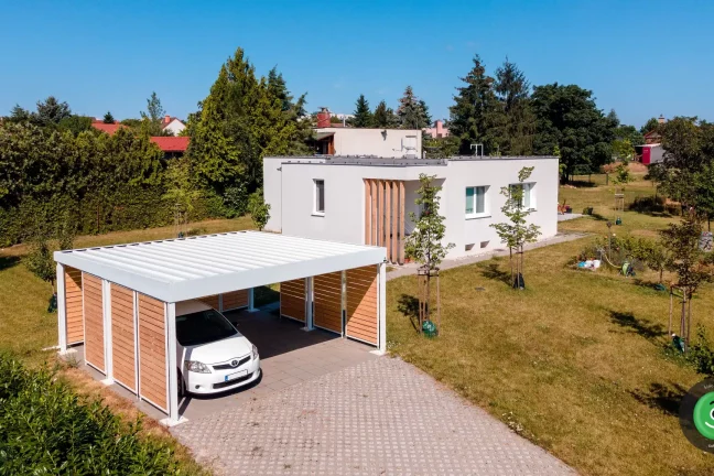 Prístrešok pre dve autá s bielou strechou medzi ovocnnými stromčekmi.