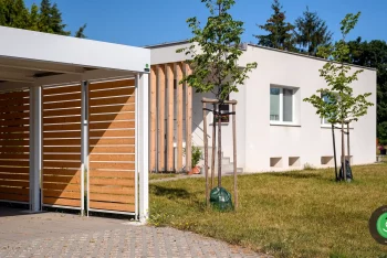 Prístrešok GARDEON s bielou strechou pri bielom rodinnom dome.