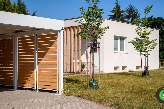 Prístrešok GARDEON s bielou strechou pri bielom rodinnom dome.