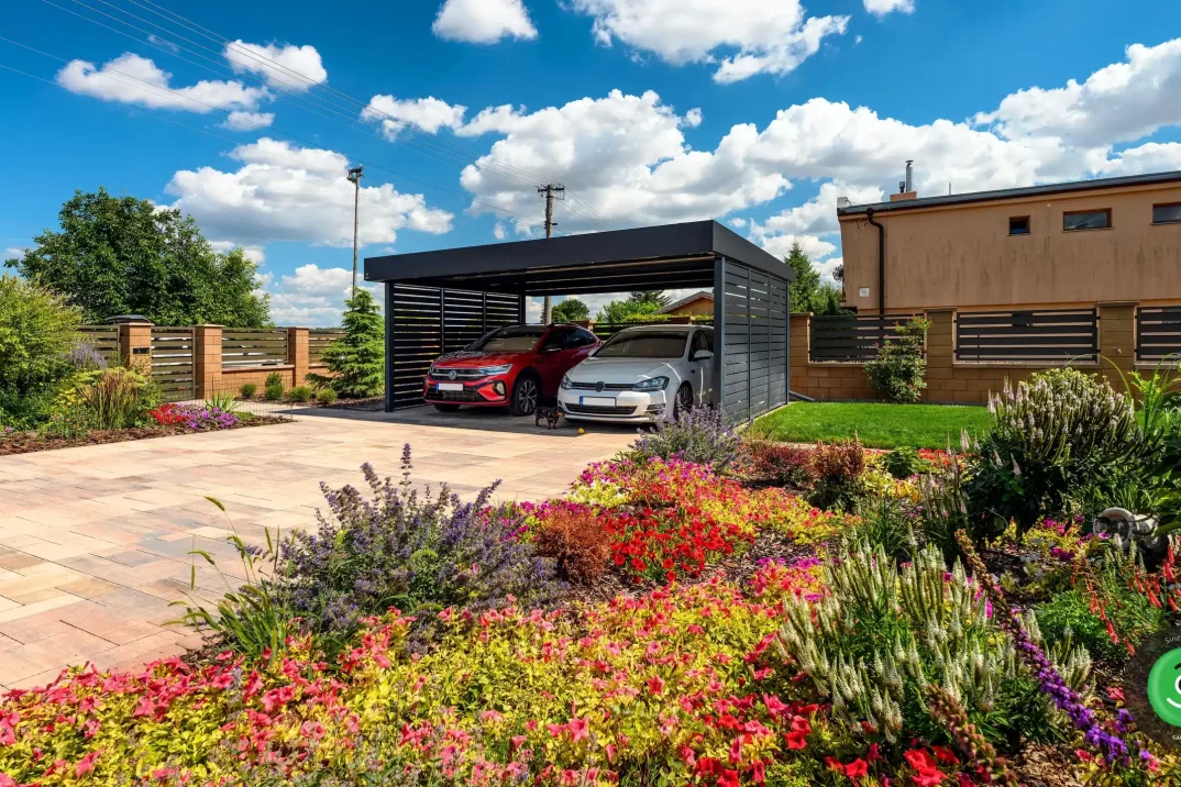 Prístrešok pre autá na zámkovej dlažbe obklopený kvetinovou záhradou.