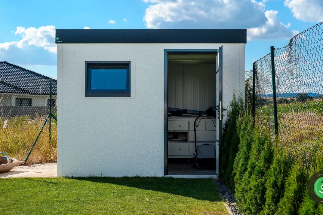 Malý biely záhradný domček s čiernou atikou.