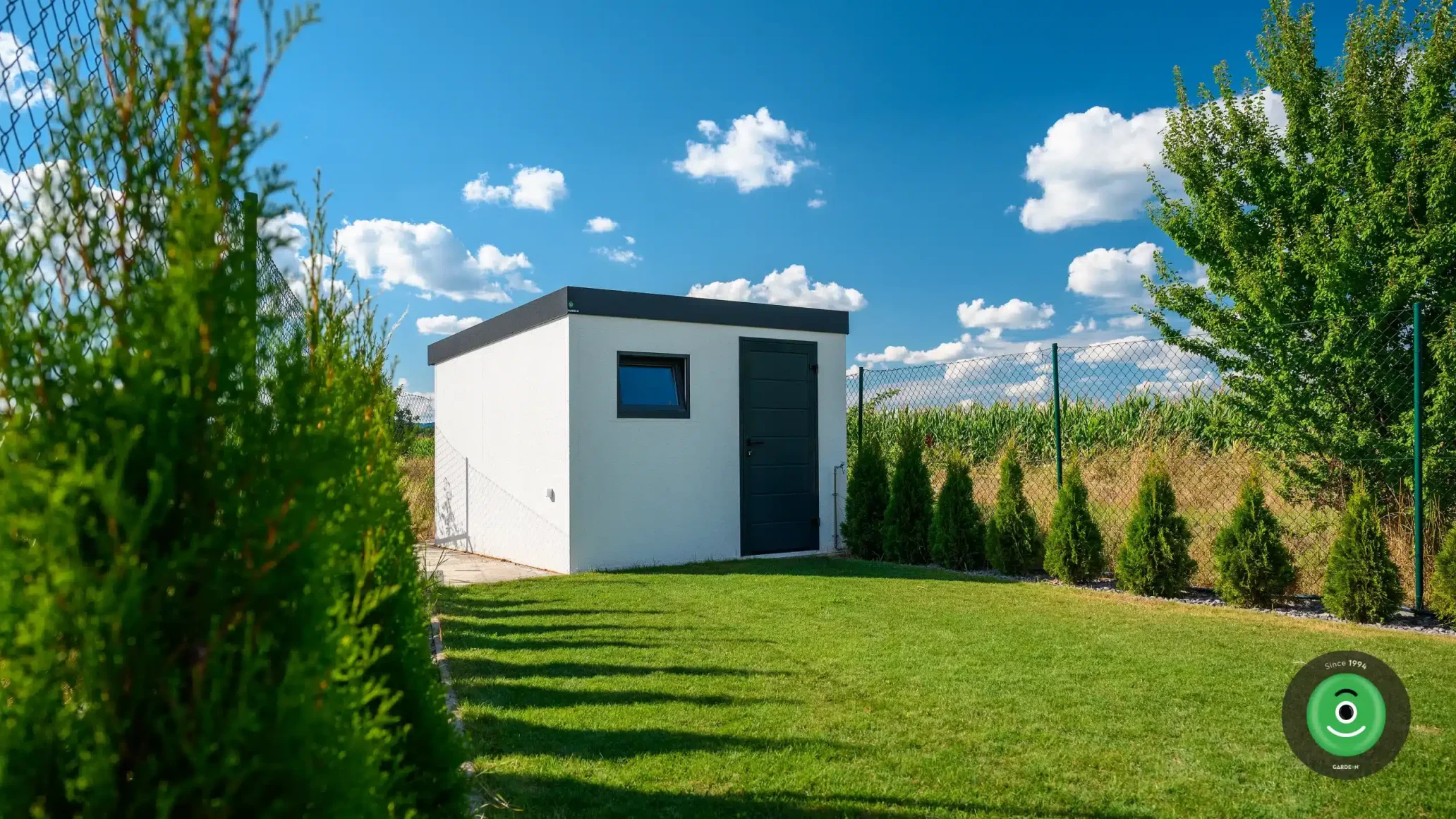 Biely GARDEON záhradný domček obklopený stromčekmi.