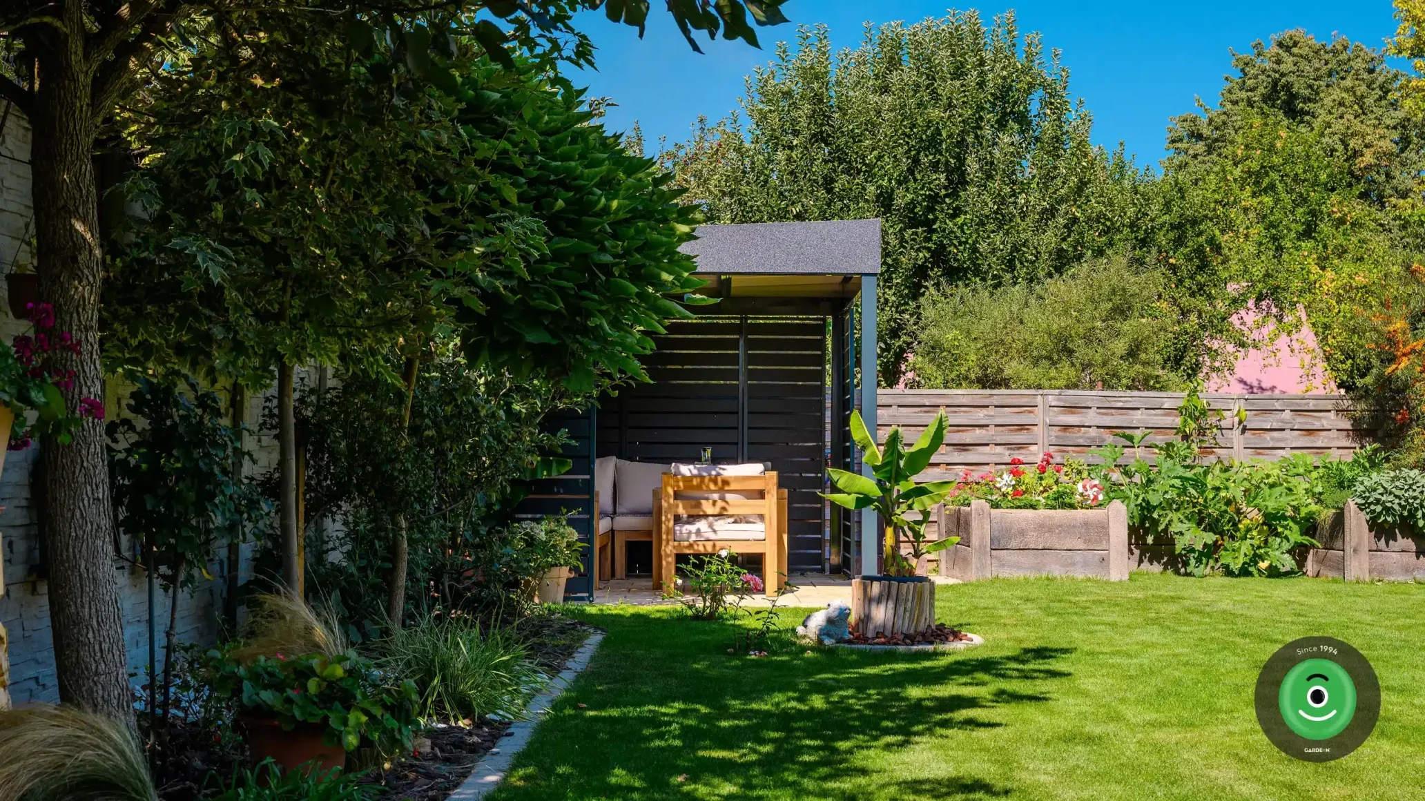 Gardeon pergola s posedením obklopená stromami a kvetmi