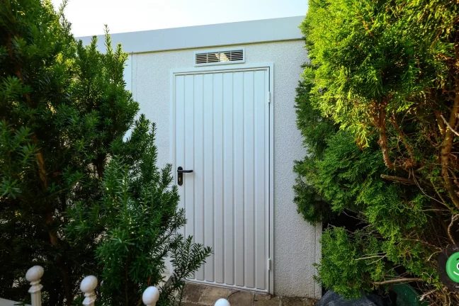 Dvere záhradného domčeka ukryté medti veľkými zelenými stromami