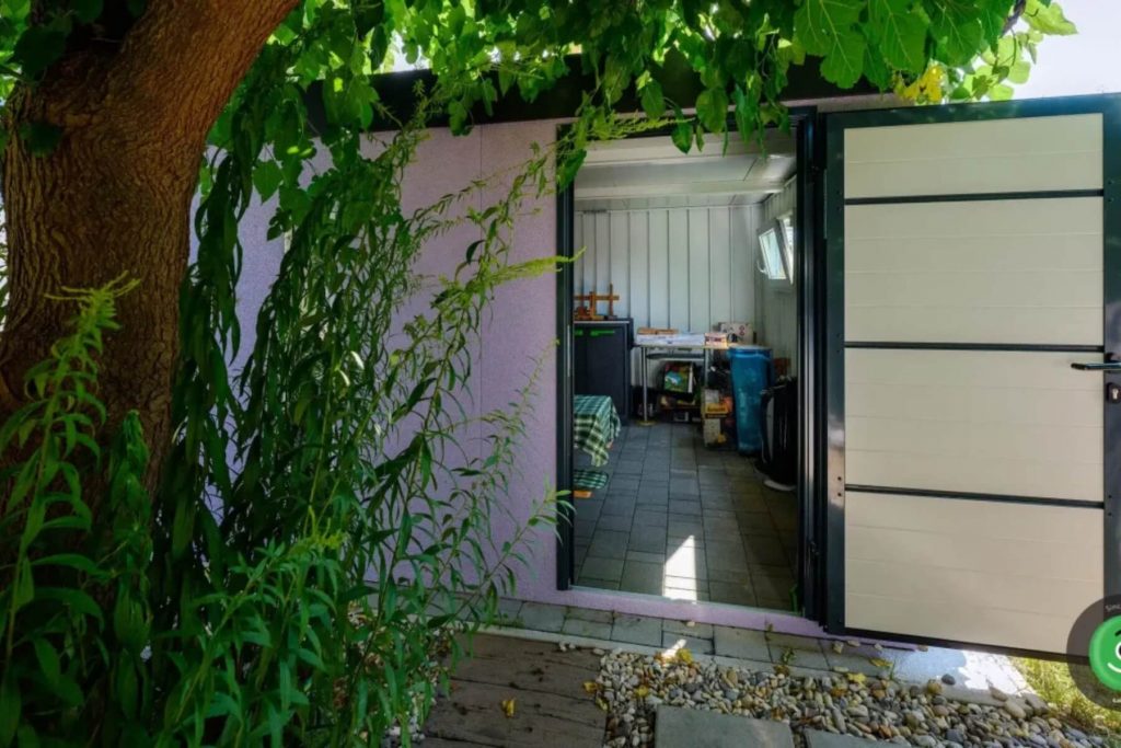 Okolie z&aacute;hradn&eacute;ho domčeka s dlažbou, kamienkami a rastlinami.