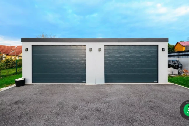 Biela dvojgaráž s čiernou širokou bránou.