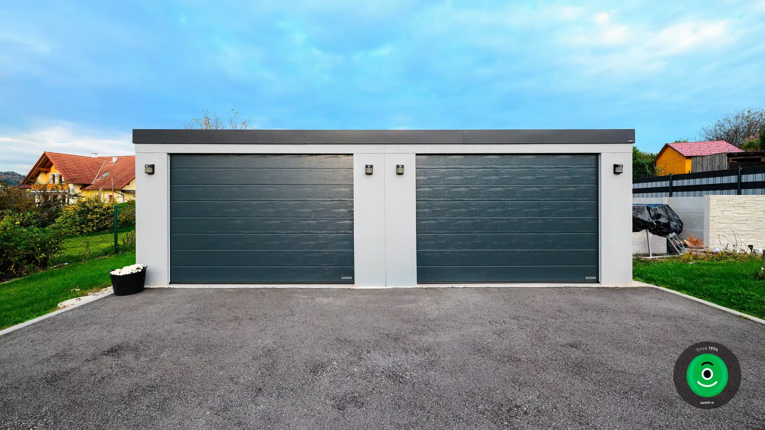 Biela dvojgaráž s čiernou širokou bránou.