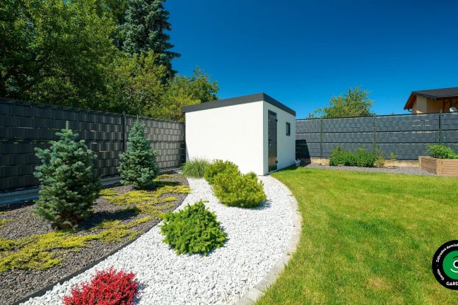 Biely záhradný domček obklopený zeleňou a kvetmi.