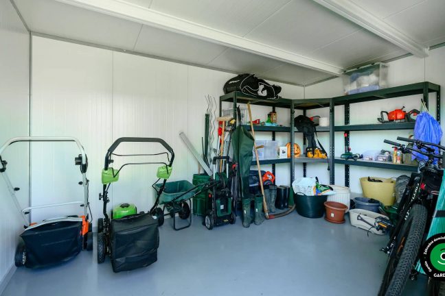 Vnútro bieleho záhradného domčeku s odleženými záhradnými vecami.