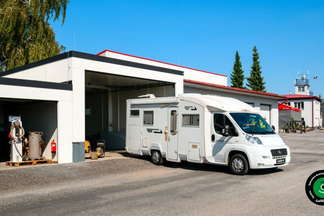 Atypická stavba garáže s otvorenými bránami a parkovanými vozidlami.