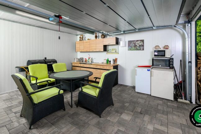 Estetický záhradný domček s garážovou bránou a kuchyňou vo vnútri.