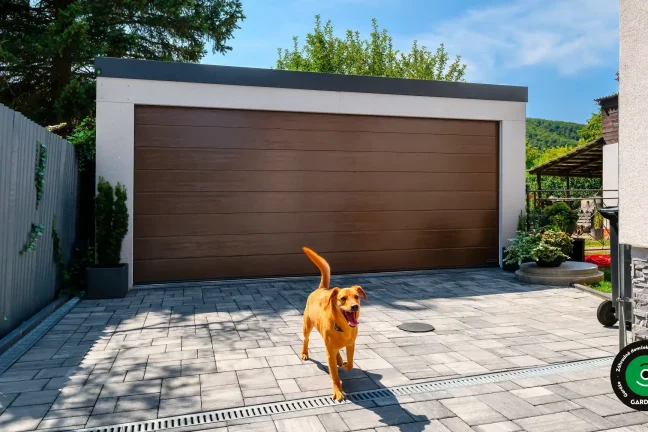 Moderná dvojgaráž s hnedou bránou a psom na dvore.