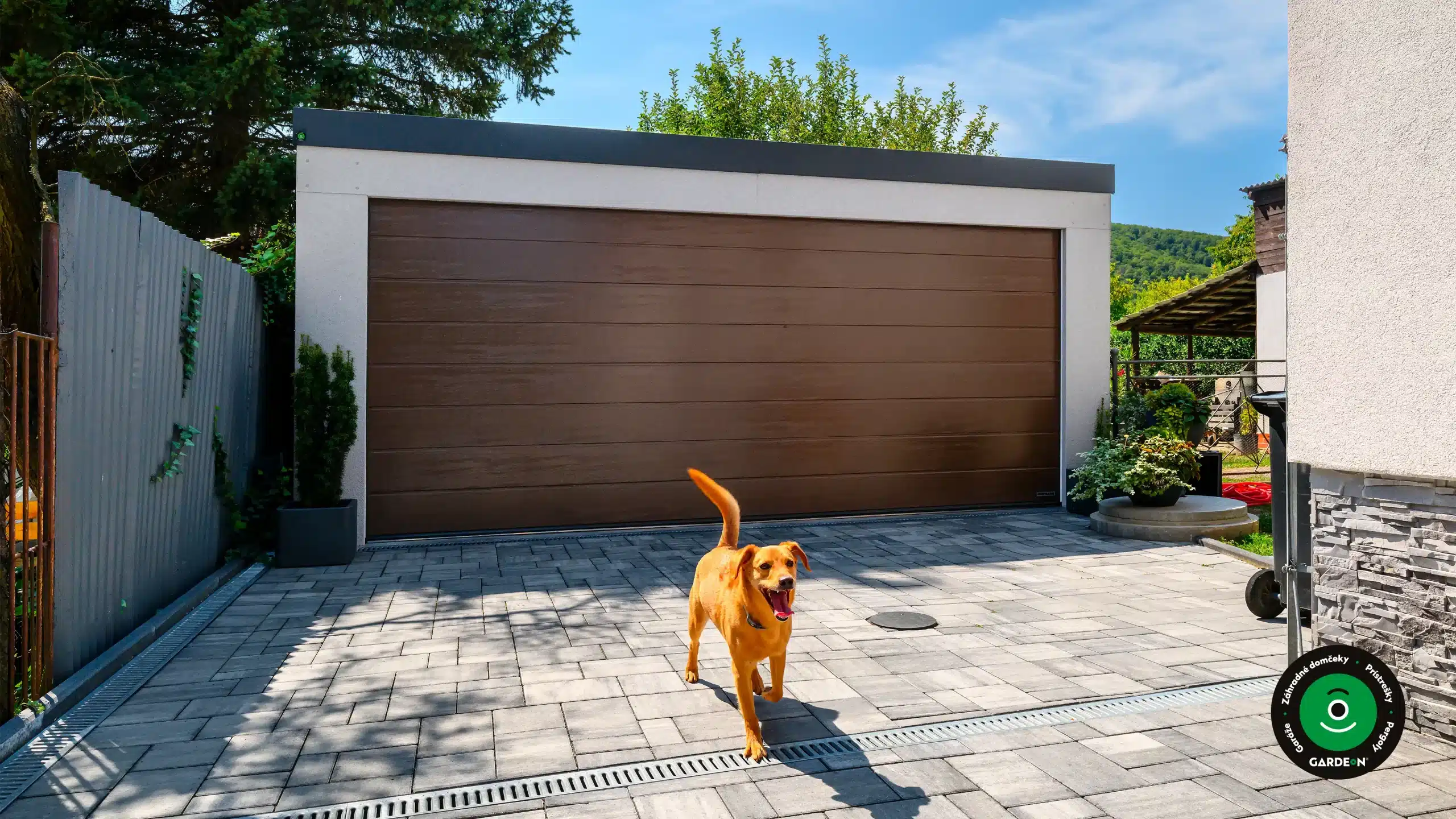 Moderná dvojgaráž s hnedou bránou a psom na dvore.