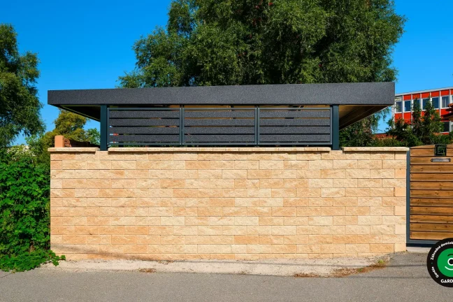 Pohľad zvonku na prístrešok ukrytý za kamenným múrom.