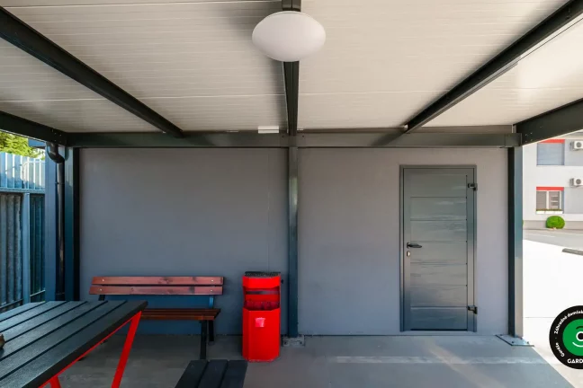 Zastrešený priestor so stolom a lavičkami pri garážach.