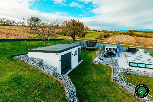 Garáž na svahu obklopená gabionmi a udržiavaným zeleným trávnikom