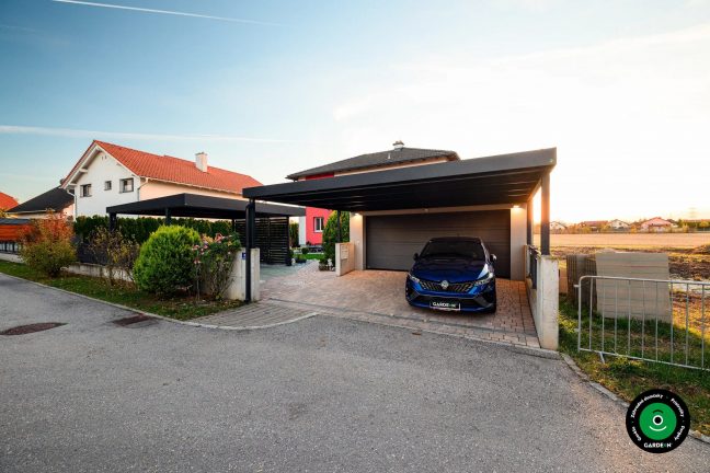 Moderná garáž s prístreškom pri dome s upravenou predzáhradkou a kríkmi