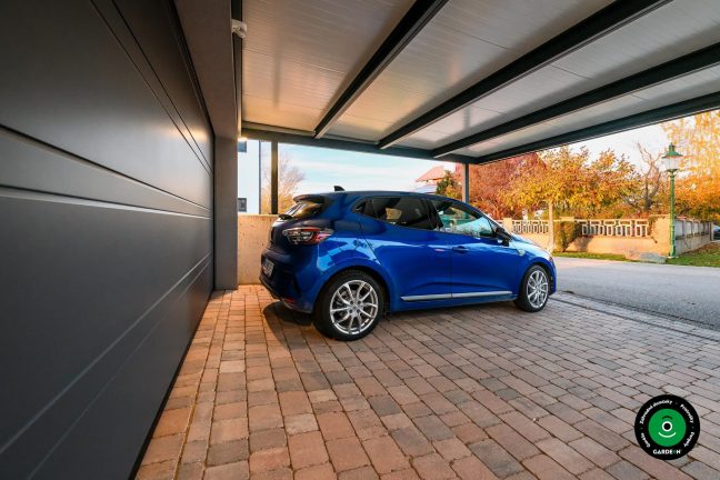 Modré auto pod prístreškom pri veľkej garáži