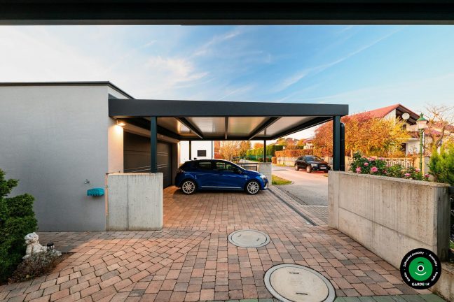 Auto pod prístreškom pri betónovej stene a záhrade