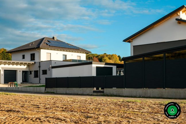 Moderná garáž pri rodinnom dome s tmavým plotovým oplotením
